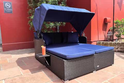 Outdoor daybed with retractable blue canopy on brick patio beside red wall