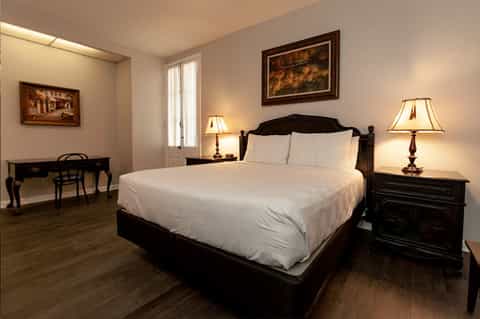 Elegant bedroom with black four-poster bed, white linens, dark wood nightstands, and framed artwork on beige walls