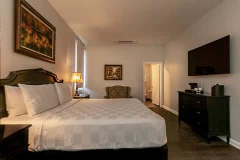 Spacious hotel bedroom with queen bed, dark headboard, TV, and elegant neutral furnishings
