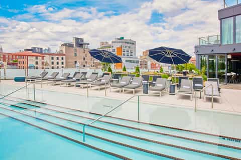 Rooftop pool deck with lap lanes, lounge chairs, navy umbrellas, and city skyline views