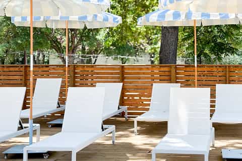 Outdoor deck with white loungers, blue and white striped umbrellas, wooden fence, and shaded seating area