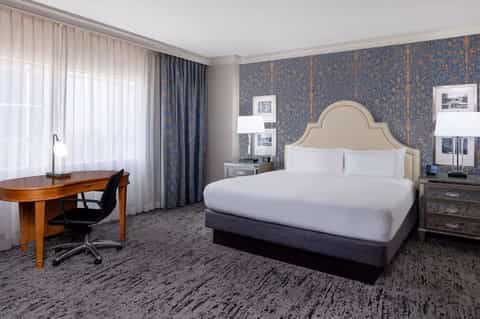 Upscale hotel bedroom with blue patterned wallpaper, king bed, work desk, and elegant furnishings
