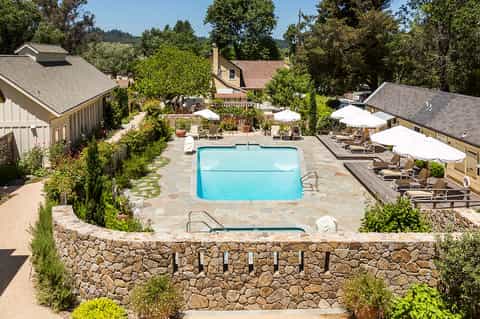 Resort pool surrounded by stone walls, lounge chairs, and umbrella seating areas