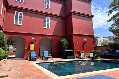 Red-walled building with arched entrances and swimming pool surrounded by lounge chairs