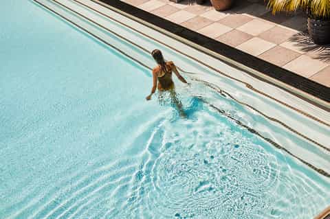 Woman swimming in outdoor pool with clear blue water and tiled deck