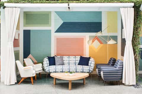 Modern lounge area with colorful geometric mural, patterned sofa, and mid-century armchairs around wooden coffee table