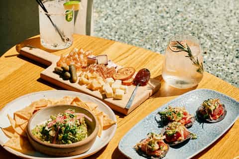 Upscale charcuterie board with cheeses, meats, and appetizers beside cocktails