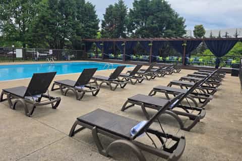 Large outdoor swimming pool with black loungers, white umbrellas, pergola shade structures, and mountain views