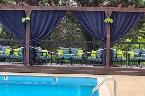 Poolside pergola with navy curtains, patterned lounge chairs, and hanging planters overlooking trees