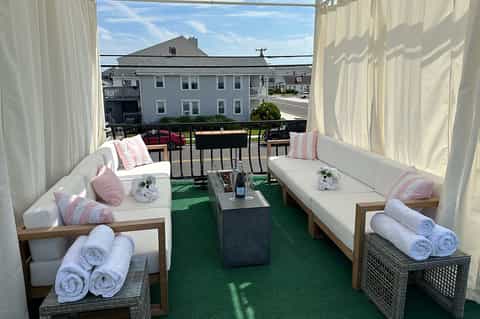 Outdoor terrace with white curtains, seating areas with pink and white pillows, rolled towels, and ocean view backdrop