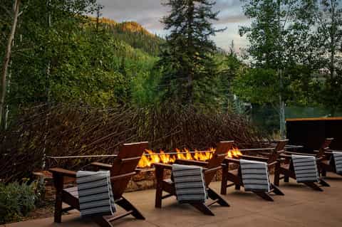 Outdoor fire pit lounge with Adirondack chairs surrounded by mountain forest landscape