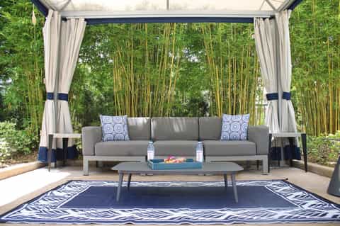 Covered outdoor lounge area with gray sofa, decorative pillows, and bamboo forest backdrop