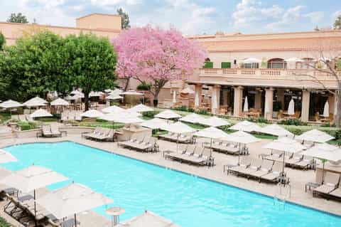 Luxury resort courtyard with pool, white umbrellas, lounge chairs, and pink flowering trees