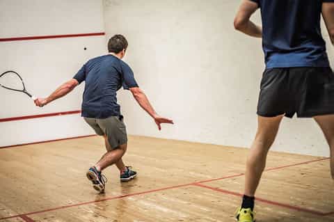 Two men playing squash in an indoor court with red lines on wooden floor