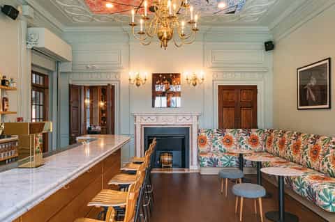 Elegant hotel bar interior with marble countertop, ornate chandelier, fireplace, and patterned seating