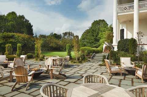 Elegant outdoor patio with Adirondack chairs, stone pathways, manicured hedges, and white colonial mansion