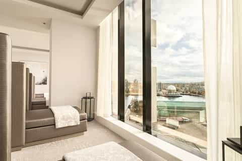 Luxury hotel bedroom with floor-to-ceiling windows overlooking cityscape with river and waterfront