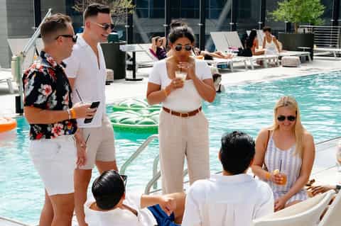 Group of guests socializing by a resort pool with lounge chairs and modern architecture in background