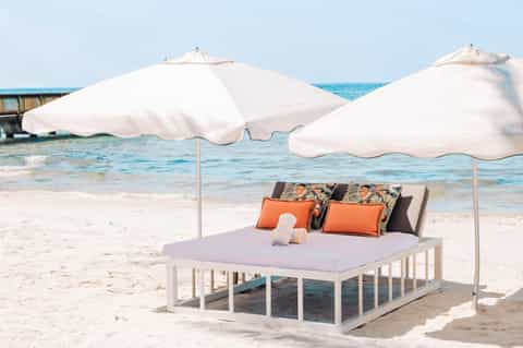 Beach bed with white umbrellas, orange and patterned pillows overlooking turquoise ocean water