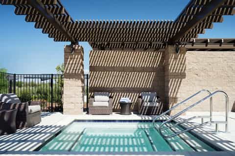 Modern pergola-covered patio with pool, lounge seating, and stone accent wall under clear blue sky