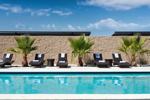 Resort swimming pool with turquoise water, black lounge chairs, palm trees, and stone accent wall