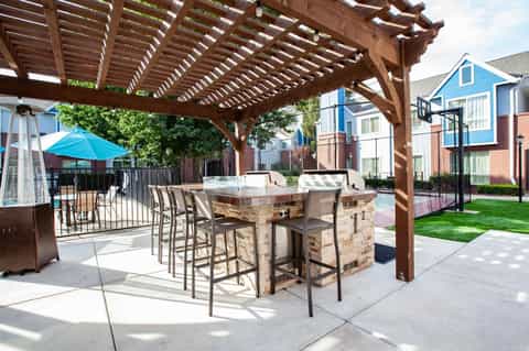Outdoor patio with stone bar, wooden pergola, blue umbrella, and residential buildings