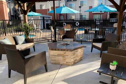 Outdoor patio with wicker chairs, fire pit, umbrellas, and pool view surrounded by residential buildings