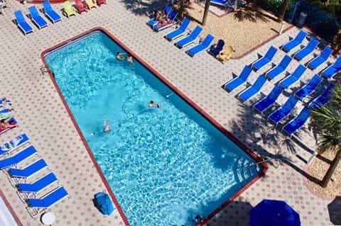 Rectangular hotel pool with clear blue water surrounded by blue lounge chairs and sandy deck area