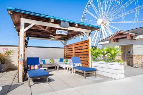 Beachfront deck with pergola, blue lounge chairs, striped cushions, and Ferris wheel view