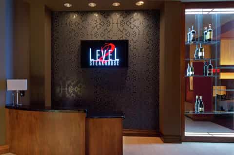 Upscale steakhouse reception area with neon sign, patterned wallpaper, wooden desk, and wine display