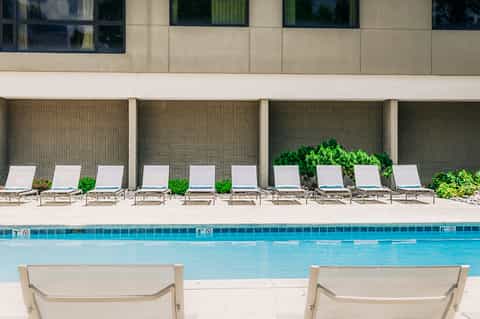 Resort pool with white lounge chairs arranged along concrete deck and modern building backdrop
