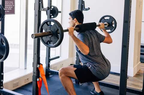Man performing barbell squat exercise in gym with weight plates and mirrors
