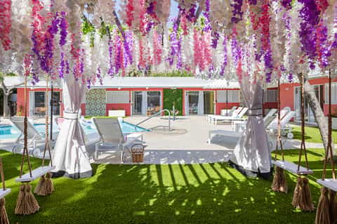 Outdoor garden venue with hanging purple and pink wisteria flowers, lounge chairs, and pool area