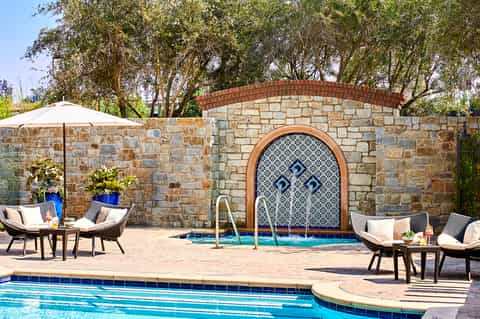 Spa area with decorative stone wall, Moroccan-style archway, lounge chairs, and umbrella by small pool