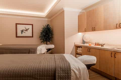 Spa treatment room with massage tables, wooden cabinetry, and warm ambient lighting
