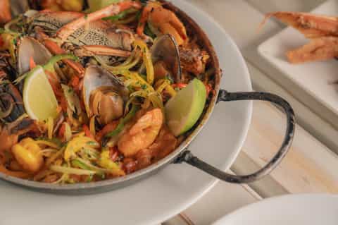 Paella seafood dish with mussels, shrimp, and vegetables in a metal pan with lime garnish