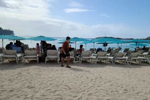Beach scene with turquoise umbrellas, lounge chairs, and guests relaxing by the sea