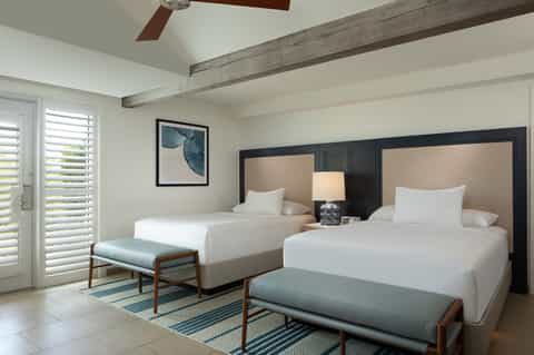 Spacious hotel room with two queen beds, neutral bedding, and modern furnishings