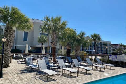 Resort pool deck with lounge chairs, palm trees, and modern buildings under clear blue sky