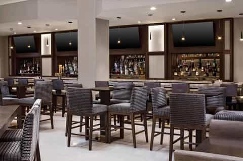 Modern bar lounge with dark wood cabinetry, pendant lighting, striped upholstered seating, and backlit shelves
