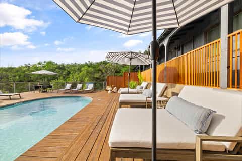 Daytime resort pool on wooden deck with striped umbrellas, lounge chairs, orange railing, and forested landscape views