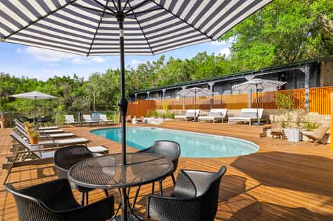 Resort pool with striped umbrella and wooden deck surrounded by trees