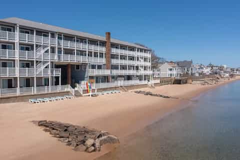 Beachfront hotel with white railings and beach loungers on sandy shore beside calm water