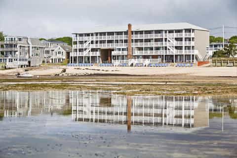 Beachfront hotel building with rows of blue loungers reflected in shallow water