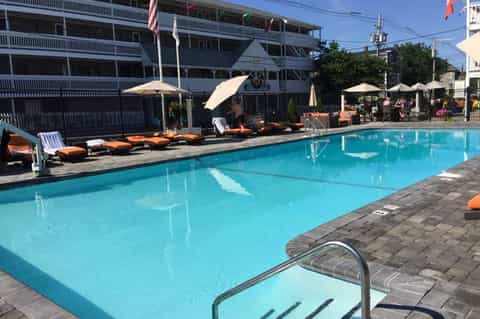 Outdoor swimming pool with lounge chairs, umbrellas, multi-story hotel building, and poolside seating