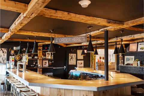 Rustic bar interior with exposed wooden beams, black pendant lights, and wooden countertop