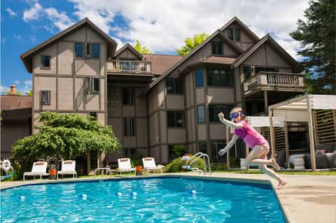 Child jumping into residential swimming pool with Tudor-style house and lounge chairs