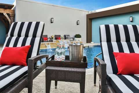 Poolside lounge area with striped black and white chaise lounges and red accent pillows