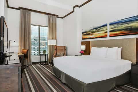 Modern hotel bedroom with king bed, work desk, and floor-to-ceiling windows with city views