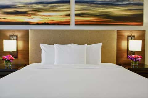 Hotel bedroom with queen bed, sunset artwork above headboard, and modern lighting
